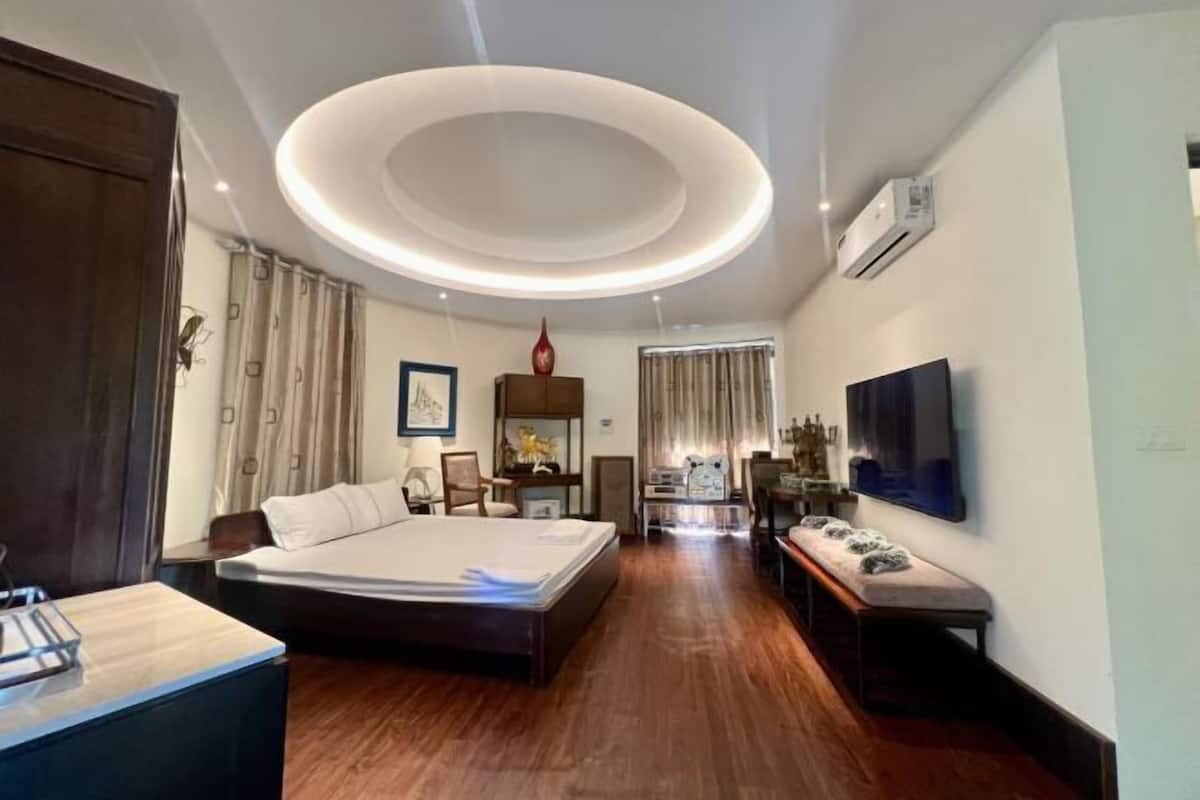 A modern hotel room with a large bed, a desk, a TV, and a circular ceiling light.