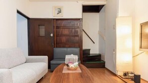 Una sala de estar con un sofá, una mesa de centro con una cesta, un sillón gris, una puerta de madera y una escalera.