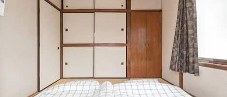 A room with a bed, a wooden wardrobe, and a window with a curtain.