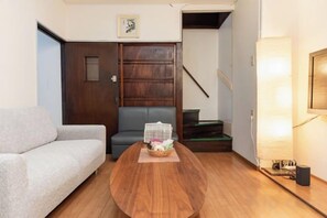Una sala de estar con un sofá, una mesa de centro de madera, una mesa pequeña con una cesta, una puerta y una escalera.