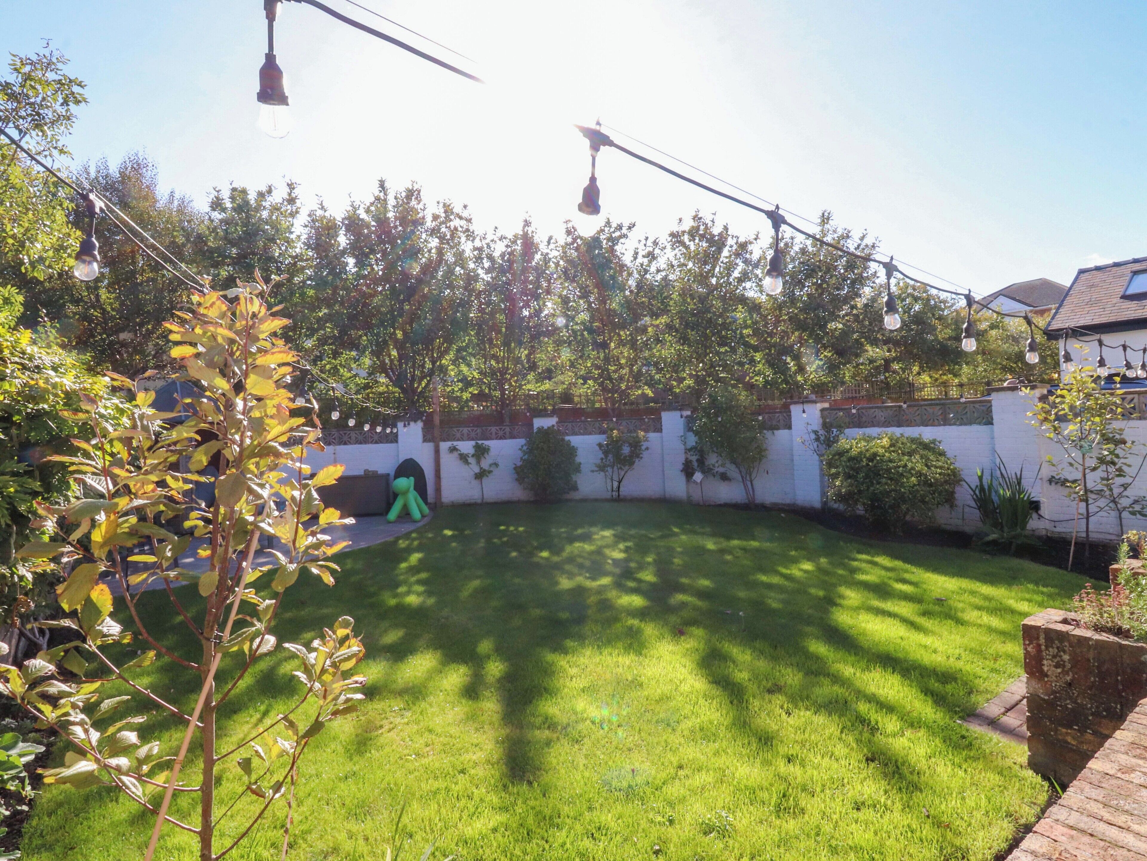 Un jardin avec un mur blanc, une pelouse verdoyante et des luminaires suspendus.