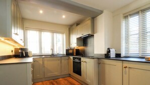 A kitchen with light-colored cabinets, a wooden floor, and a built-in oven. - Gardener's Cottage (Lytham St. Anne's)