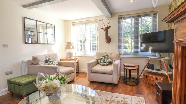 A living room with a glass coffee table, two armchairs, a sofa, a television, and a mounted deer head. - Gardener's Cottage (Lytham St. Anne's)