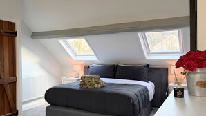 A bedroom with a skylight, a bed with a patterned throw, and a vase of red roses on a nightstand. - Gardener's Cottage (Lytham St. Anne's)