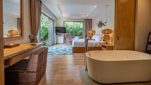 A modern hotel room with a large bed, a bathtub, a desk with a chair, a TV, and a view of greenery outside. - Villa Allamanda 3 Bdrm Best Location Bangtao Beach VVPHU88 (Phuket)