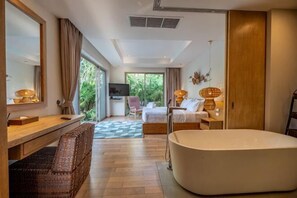 A modern hotel room with a large bed, a bathtub, a desk with a chair, a TV, and a view of greenery outside. - Villa Allamanda 3 Bdrm Best Location Bangtao Beach VVPHU88 (Phuket)