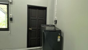 Une pièce avec une porte noire, une fenêtre et un appareil électroménager noir, peut-être un réfrigérateur ou un lave-linge, le tout adossé au mur.