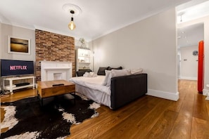 A modern living room with a fireplace, a sofa, a TV, and a wooden floor. - Exclusive 1 bedroom Apartment in Hackney! (London)