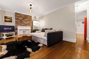 A modern living room with a fireplace, a sofa, a TV, and a brick accent wall. - Exclusive 1 bedroom Apartment in Hackney! (London)