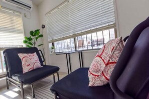 Ein Zimmer mit einem schwarzen Stuhl, einem Fenster mit Jalousien und einem Blumentopf.