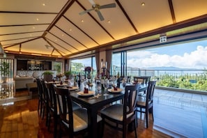 A dining area with a large table set for a meal, a ceiling fan, and a view of the outdoors.