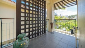 A balcony with a view of greenery and buildings, a decorative owl sculpture, and a metal railing. - Amano Terrace (Onna)