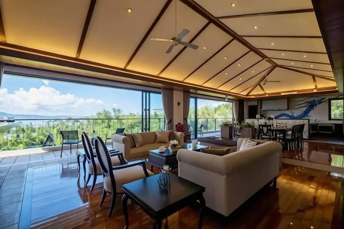 A spacious living area with a high ceiling, large windows, and a view of the outdoors.