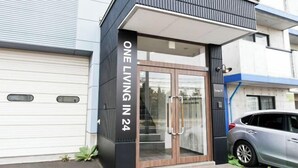 En moderne bygningseingang med en glasdør, et skilt med teksten 'ONE LIVING IN 24', og en bil parkeret udenfor.