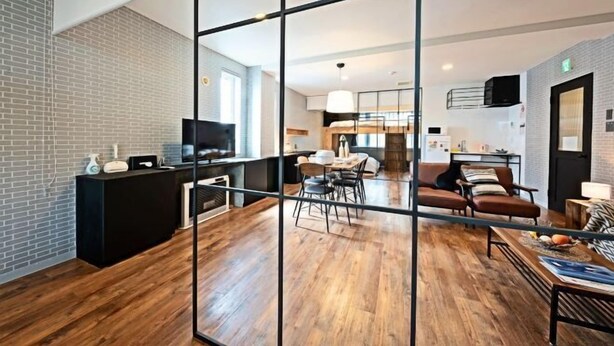 Et moderne hotelværelse med trægulv, sort receptionsdisk, fladskærms-tv, et spiseområde med bord og stole samt en opholdsstue med sofa og sofabord.