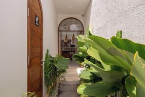 A narrow hallway with a wooden door and large green plants. - Sueño Villa Seminyak (Bali)
