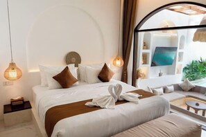 A hotel room with a bed, a sofa, a small table, and a large window with a view. - Sueño Villa Seminyak (Bali)