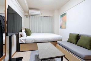 A compact hotel room with a bed, a sofa, a TV, and a painting on the wall. - Access Bunkyo Otsuka (Tokyo)