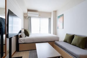 A compact room with a bed, a sofa, a flat-screen TV, and an air conditioning unit. - Access Bunkyo Otsuka (Tokyo)