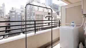 A balcony with a city view, a water dispenser, and a window with a metal guard. - Shinjuku Kabukicho Harmony Inn (Tokyo)