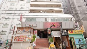 A multi-story building with a ground-floor entrance, a staircase leading to the second floor, and various signs and advertisements on the facade. - Shinjuku Kabukicho Harmony Inn (Tokyo)