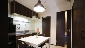 A compact kitchen with dark cabinetry, a white countertop, a black refrigerator, and a pendant light above the table. - Shinjuku Kabukicho Harmony Inn (Tokyo)