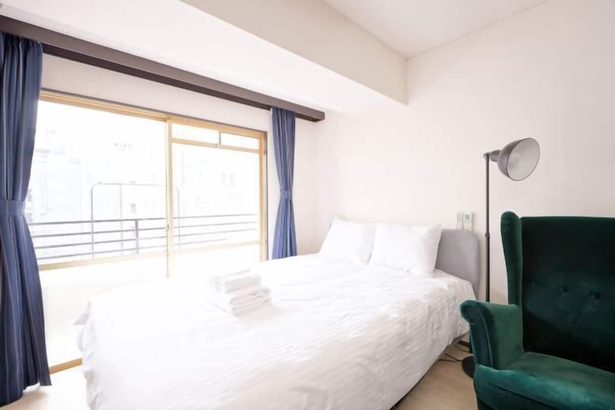 A hotel room with a large bed, a green armchair, and a floor lamp.