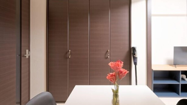 A room with a white table, a vase with flowers, a brown wardrobe, and a desk with a chair. - Shinjuku Kabukicho Harmony Inn (Tokyo)