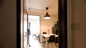 A narrow hallway leading to a dining area with a table and chairs, a hanging light fixture, and a view into another room. - Shinjuku Kabukicho Harmony Inn (Tokyo)