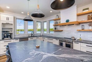 Cozinha moderna com uma ilha grande, iluminação pendente e vista para o exterior.