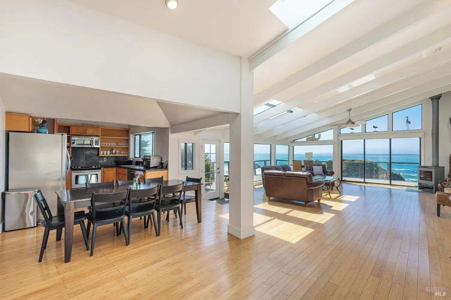 Un vaste espace de vie comprenant une grande table à manger, un coin salon confortable avec un canapé et une vue sur l’océan grâce à de grandes fenêtres.