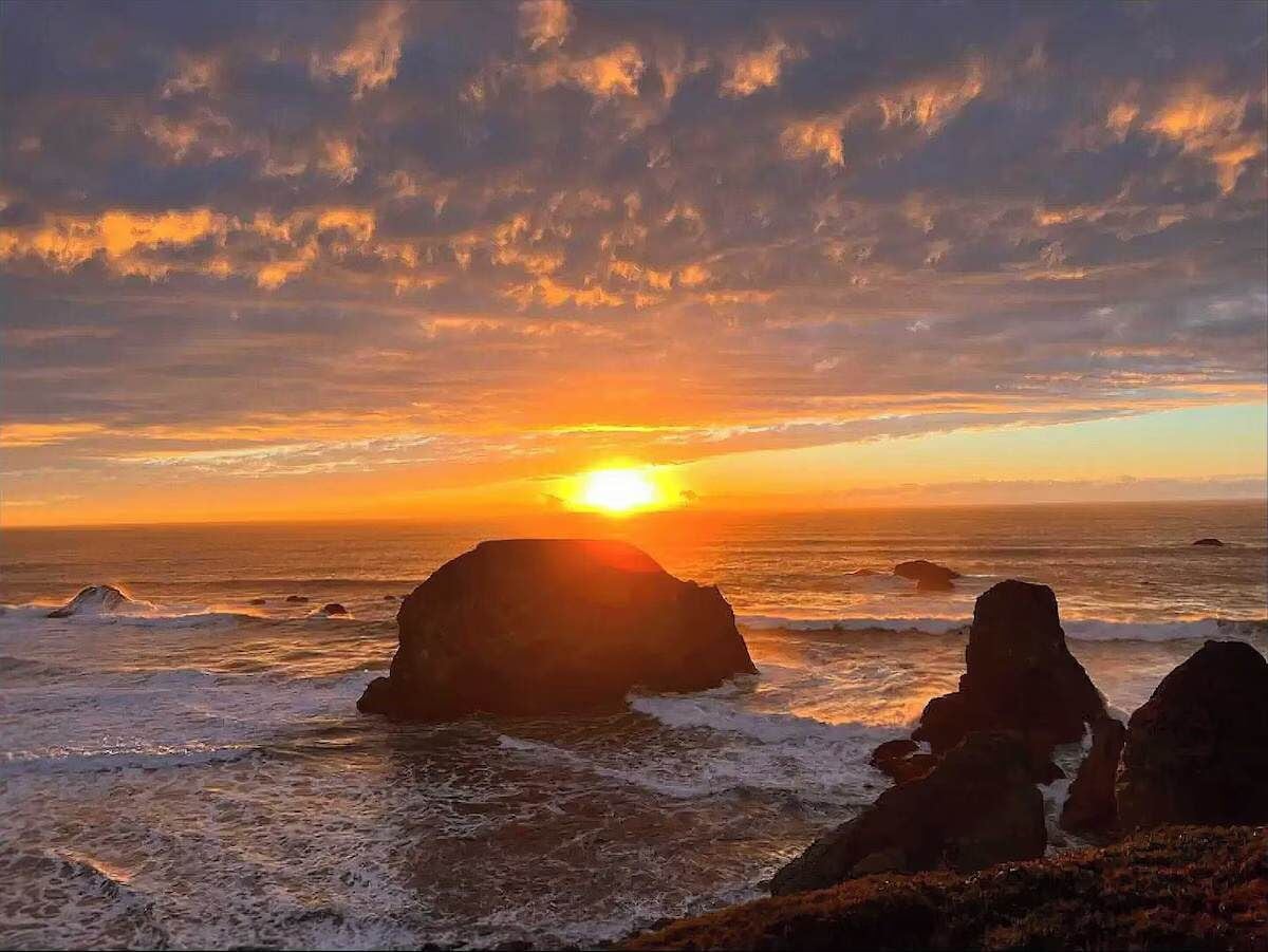 Un atardecer sobre una costa rocosa con olas rompiendo contra las rocas.
