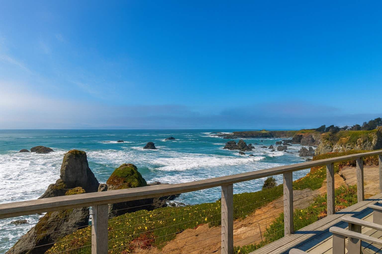A coastal view with rocky outcrops and a wooden walkway.