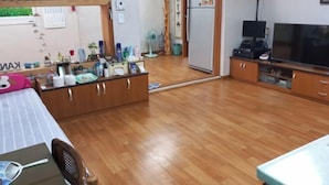 Une pièce de taille modeste comprenant un lit, une petite table, un téléviseur, un réfrigérateur et une armoire en bois.