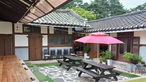Un espace extérieur aménagé dans le style traditionnel japonais, avec des tables de pique-nique en bois et un parasol rouge.