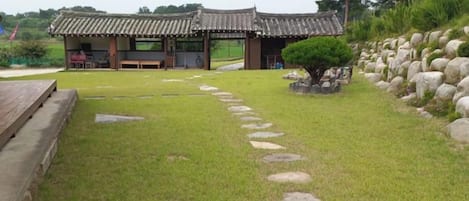 A traditional Korean-style building with a tiled roof, a stone pathway leading to the entrance, and a wooden deck on the left.