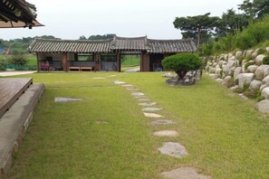 A traditional Korean-style building with a tiled roof, a stone pathway leading to the entrance, and a wooden deck on the left. - hakdonghanokpension (Gangneung-si)