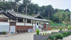 Un bâtiment de style traditionnel, doté d’un toit en tuiles, d’une façade en bois et d’un petit jardin agrémenté de plantes et d’un mur en briques.