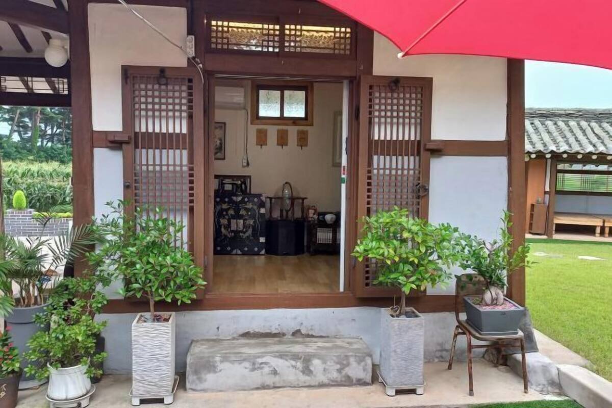 Une entrée de style japonais traditionnel, avec une porte en bois, des plantes en pot et un parapluie rouge.