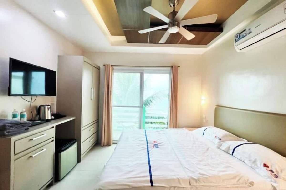 A hotel room with a bed, a TV, a ceiling fan, an air conditioner, and a window with curtains.