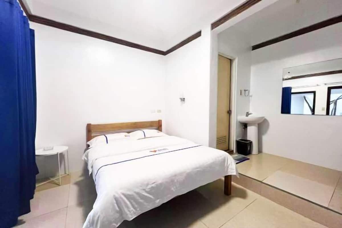 A hotel room with a bed, a small bedside table, a mirror, and a bathroom with a sink and toilet.