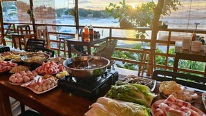 A dining area with a view of a body of water, a variety of food items on the table, and a large pot on a portable stove. - Super diving and tinas reef divers (Puerto Galera)