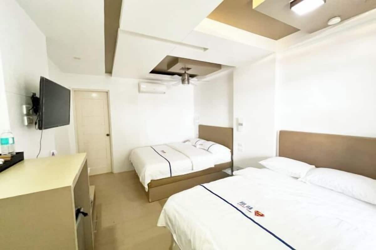 A hotel room with two beds, a desk, a TV, and a ceiling fan.