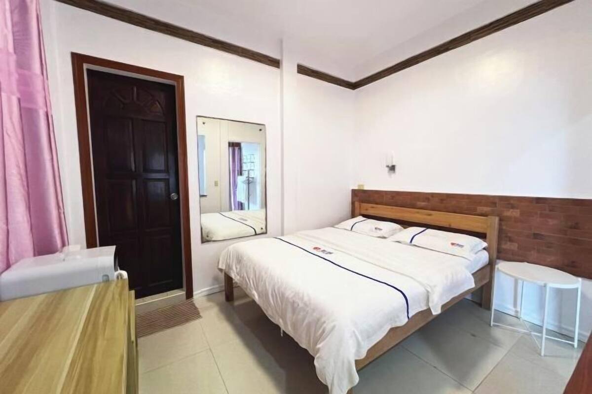 A bedroom with a wooden bed, a bedside table, a mirror, and a door.