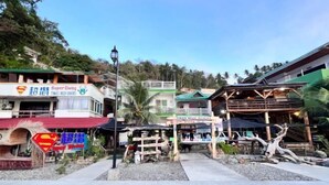 A coastal area with a Super Diving sign, a Superman sign, and a wooden structure with a tree trunk. - Super diving and tinas reef divers (Puerto Galera)