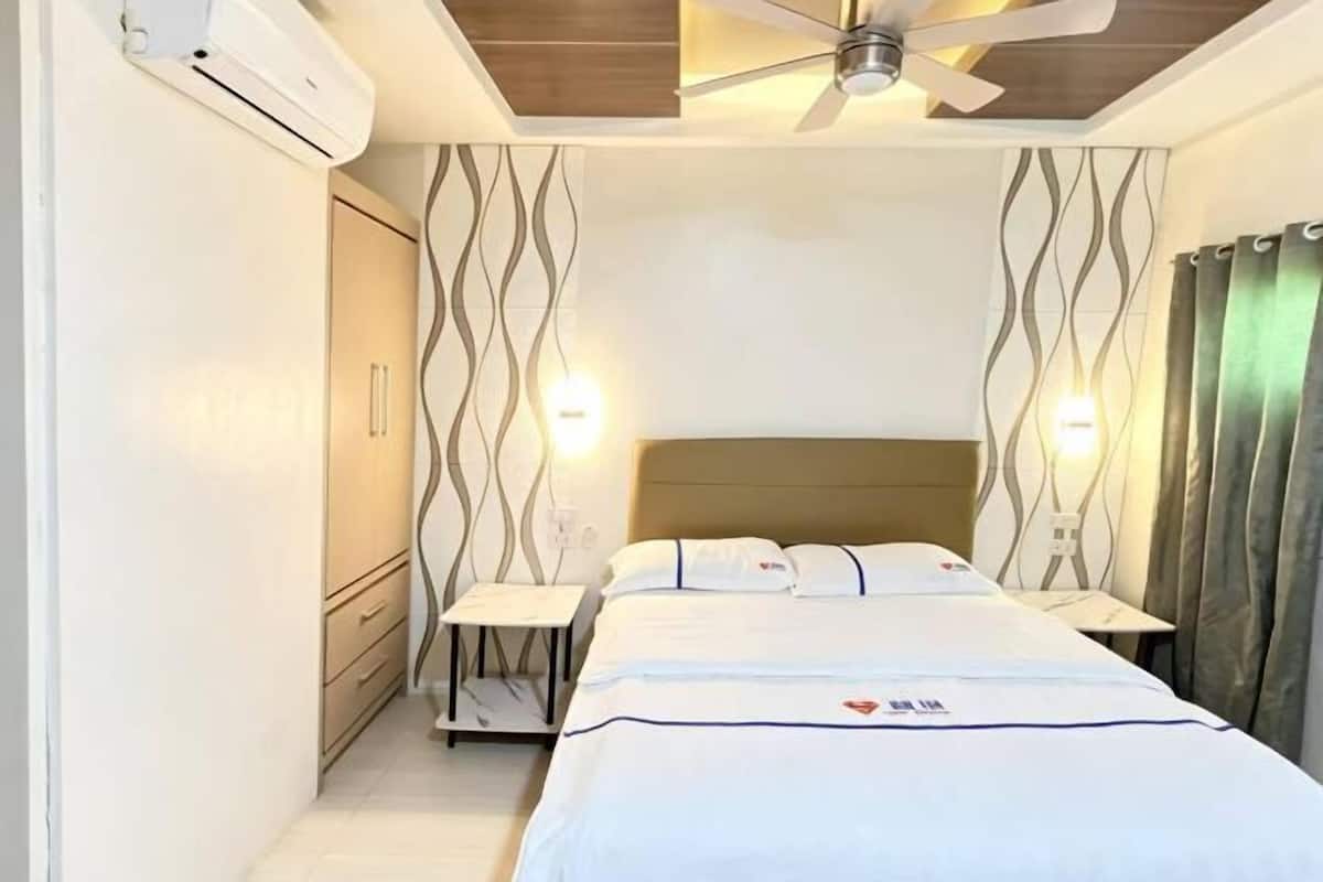 A bedroom with a bed, bedside tables, a ceiling fan, and an air conditioning unit.