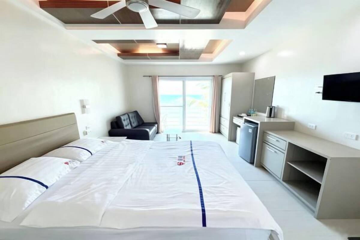 A hotel room with a bed, a desk, a TV, and a view of the outdoors.