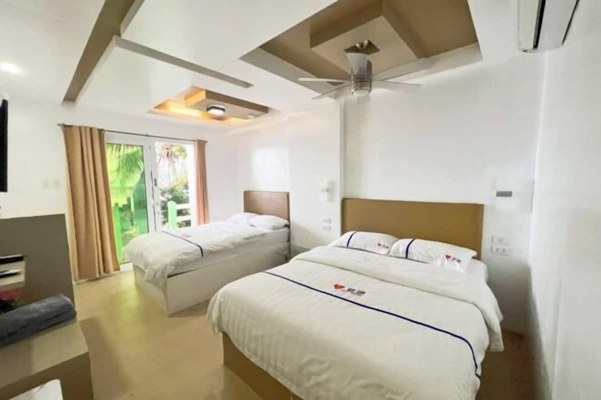 A hotel room with two beds, a ceiling fan, a TV, and a window with curtains.