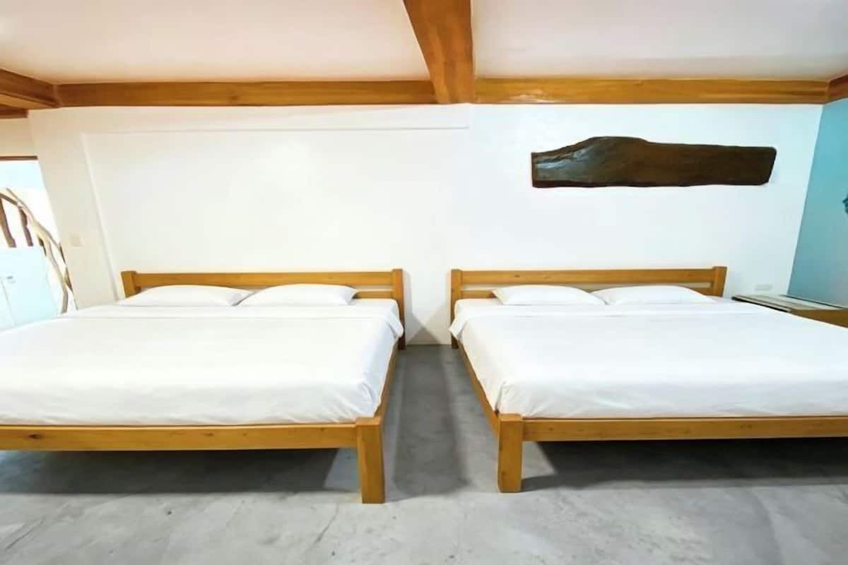A room with two wooden beds, white bedding, a wooden ceiling beam, and a wall-mounted artwork.