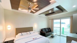 A modern hotel room with a bed, a desk, a sofa, and a balcony with a view. - Super diving and tinas reef divers (Puerto Galera)